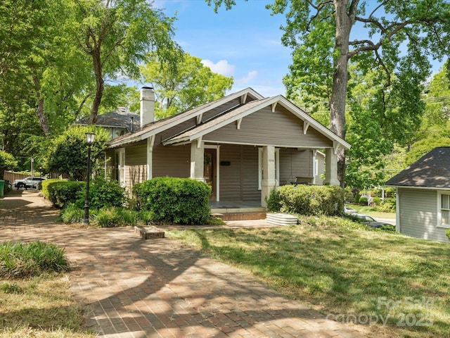 view of front of house featuring a porch, a chimney, and a front lawn