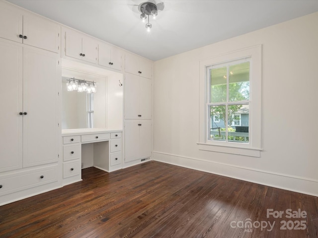 unfurnished bedroom with dark wood-style flooring, baseboards, visible vents, and built in desk
