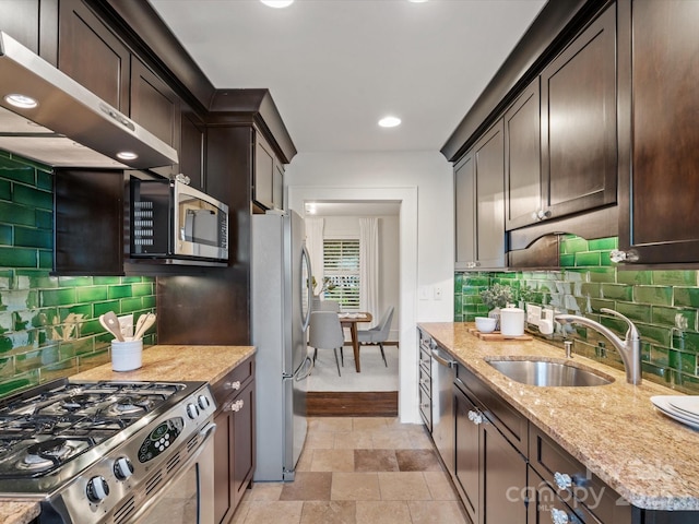 kitchen with dark brown cabinets, a sink, light stone counters, under cabinet range hood, and stainless steel appliances