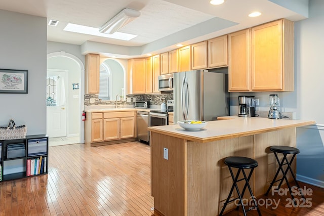 kitchen with stainless steel appliances, light wood-style floors, light brown cabinets, a kitchen bar, and a peninsula