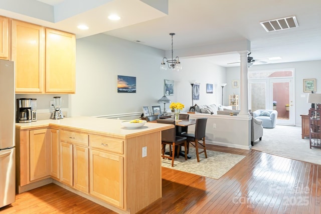 kitchen featuring light wood finished floors, light brown cabinets, visible vents, a peninsula, and freestanding refrigerator