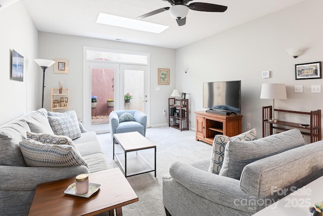living room with a ceiling fan, a skylight, light carpet, and baseboards
