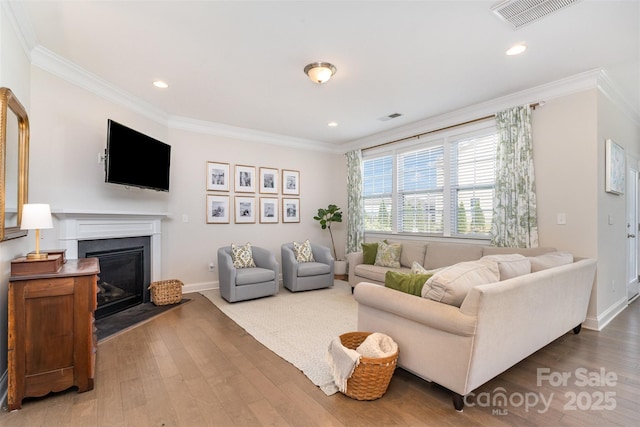 living room featuring wood finished floors, ornamental molding, a glass covered fireplace, baseboards, and recessed lighting