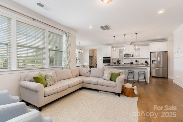 living area featuring healthy amount of natural light, crown molding, wood finished floors, recessed lighting, and a chandelier