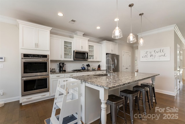 kitchen featuring stainless steel appliances, a sink, an island with sink, baseboards, and decorative backsplash