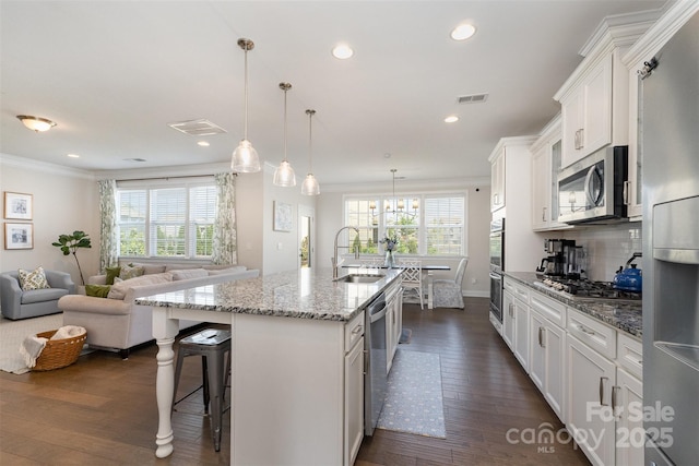 kitchen with a sink, appliances with stainless steel finishes, ornamental molding, an island with sink, and white cabinetry