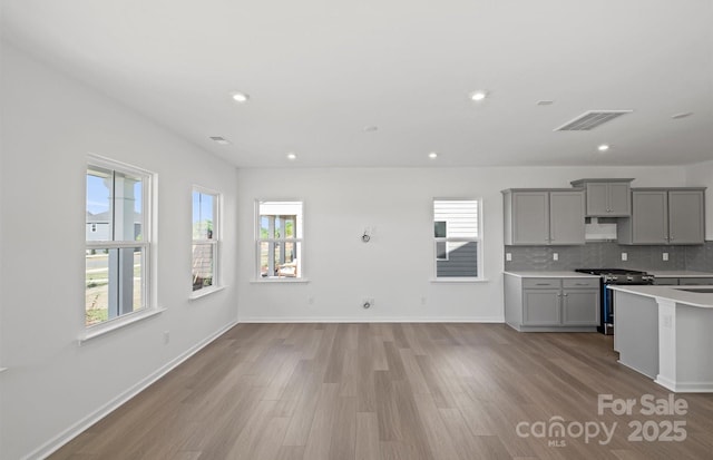 kitchen featuring a healthy amount of sunlight, gray cabinetry, gas stove, and light wood-style floors