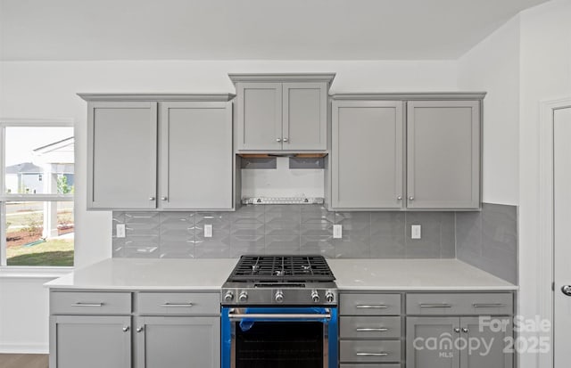 kitchen with stainless steel range with gas cooktop, light countertops, tasteful backsplash, and gray cabinets