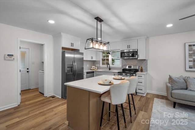 4932 Delivau Dr, Charlotte, NC 28215 - kitchen featuring appliances with stainless steel finishes, light wood-style floors, light countertops, decorative backsplash, and a kitchen bar