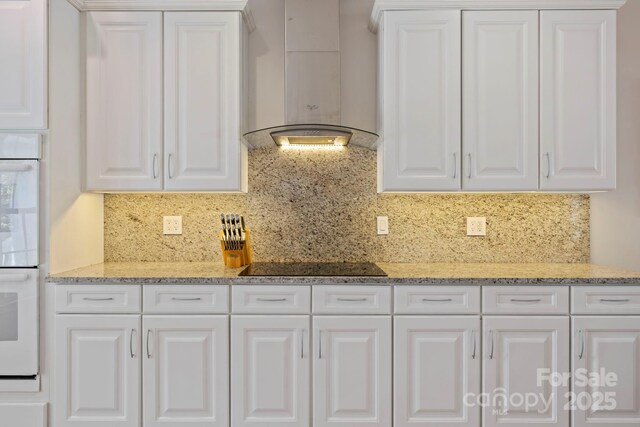 101 Skyview Dr, Asheville, NC 28804 - kitchen with wall chimney exhaust hood, black electric cooktop, white cabinetry, decorative backsplash, and light stone countertops