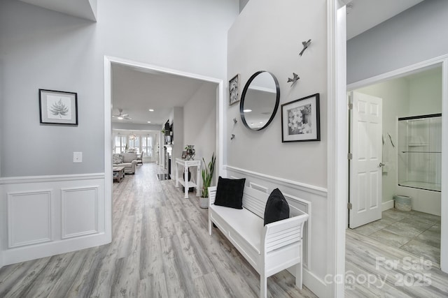 hall featuring a decorative wall, wainscoting, and wood finished floors