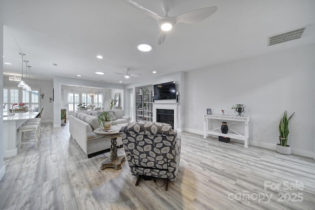 living room with baseboards, a fireplace, a ceiling fan, light wood-style floors, and visible vents