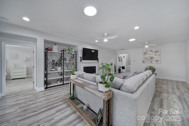 living room featuring baseboards, recessed lighting, a fireplace, a ceiling fan, and light wood-style floors