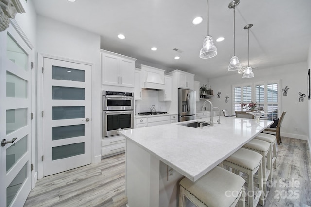 kitchen featuring a large island, white cabinets, a sink, stainless steel appliances, and custom range hood