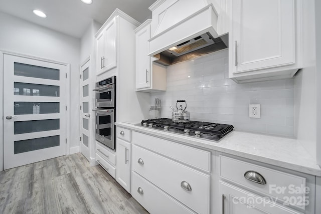 kitchen with light wood finished floors, premium range hood, white cabinetry, and appliances with stainless steel finishes