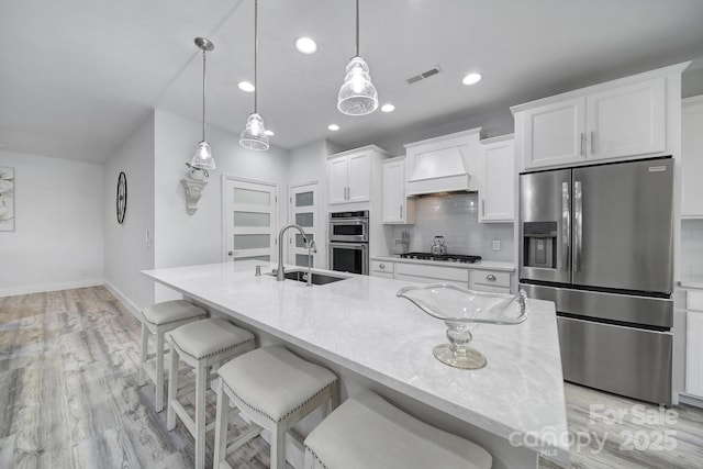 kitchen with custom range hood, backsplash, visible vents, appliances with stainless steel finishes, and a sink