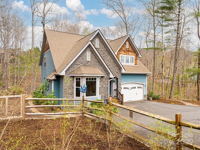 craftsman house with driveway, stone siding, a shingled roof, fence private yard, and an attached garage
