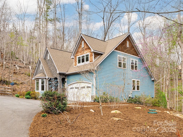 view of side of home featuring roof with shingles and aphalt driveway