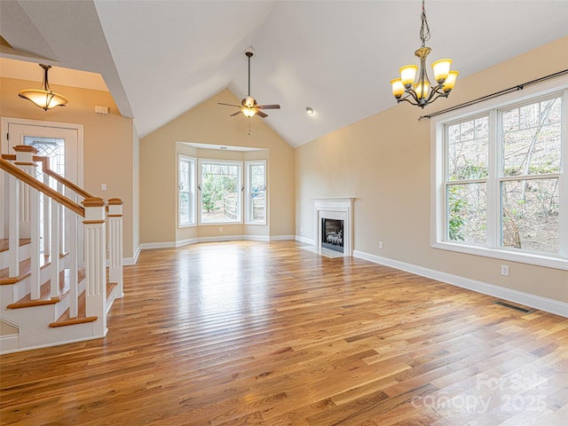 unfurnished living room featuring vaulted ceiling, stairs, ceiling fan with notable chandelier, light wood-type flooring, and visible vents