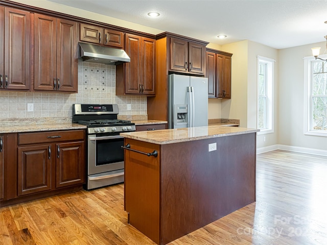 kitchen featuring stainless steel gas range, fridge with ice dispenser, light wood finished floors, backsplash, and under cabinet range hood