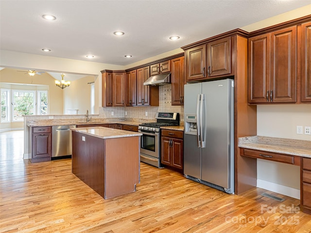 kitchen featuring a peninsula, under cabinet range hood, stainless steel appliances, and light wood finished floors