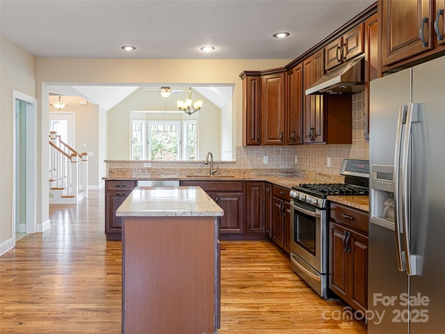 kitchen featuring light wood finished floors, under cabinet range hood, light stone countertops, a center island, and appliances with stainless steel finishes
