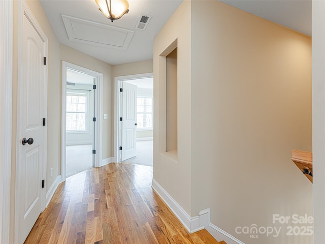 hallway with attic access, baseboards, light wood finished floors, and visible vents