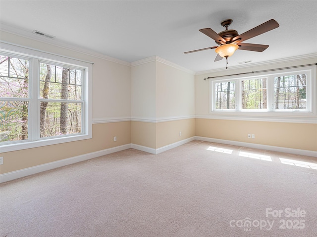 carpeted empty room featuring baseboards, a ceiling fan, visible vents, and crown molding
