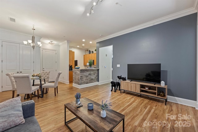 living area with visible vents, baseboards, light wood finished floors, ornamental molding, and a notable chandelier