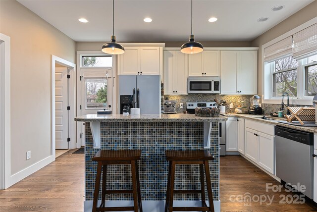 kitchen with backsplash, white cabinets, a kitchen bar, stainless steel appliances, and a sink
