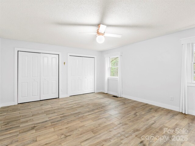 373 Vineyard Rd, Tryon, NC 28782 - unfurnished bedroom with multiple closets, light wood-type flooring, a textured ceiling, baseboards, and a ceiling fan