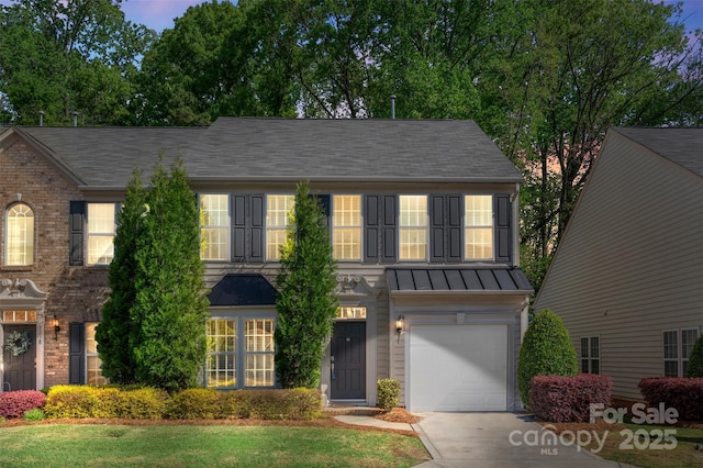 colonial home featuring a standing seam roof, an attached garage, metal roof, brick siding, and driveway
