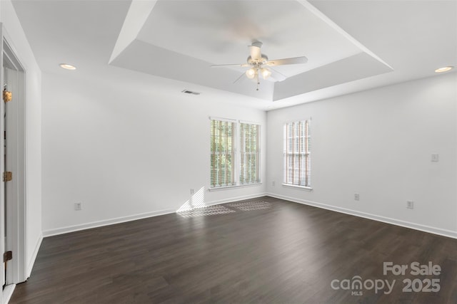 empty room with a tray ceiling, ceiling fan, baseboards, and dark wood-style floors