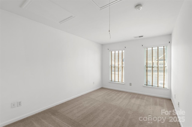 carpeted spare room with visible vents, baseboards, and attic access