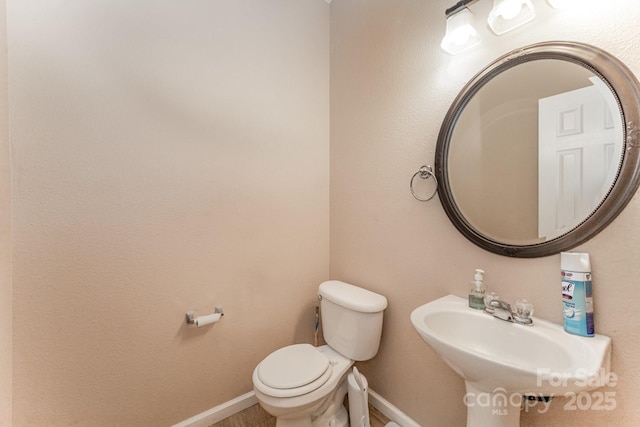half bathroom featuring toilet, baseboards, and a sink