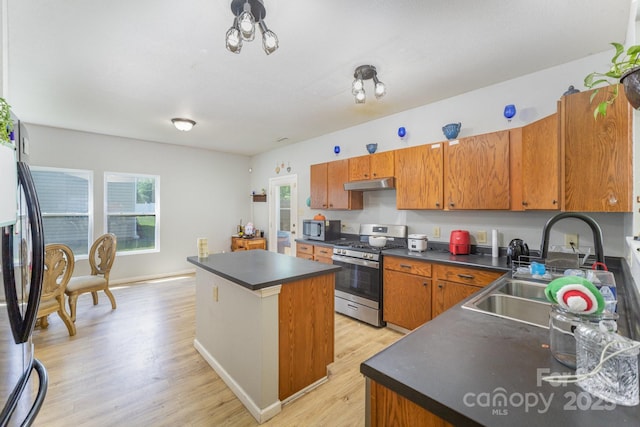 kitchen featuring under cabinet range hood, light wood finished floors, a center island, dark countertops, and appliances with stainless steel finishes