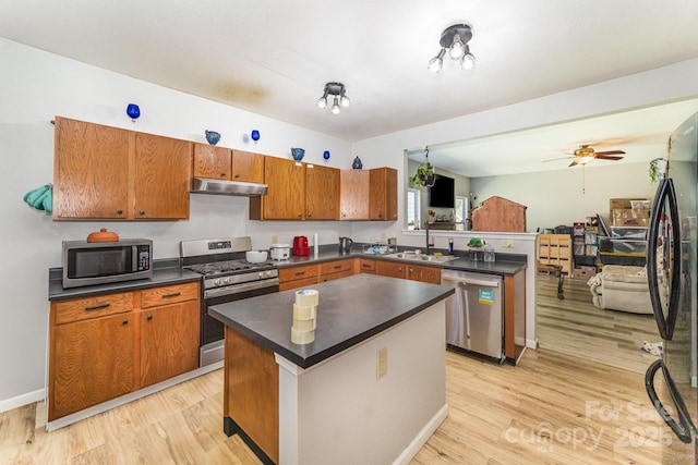 kitchen with light wood finished floors, a peninsula, dark countertops, under cabinet range hood, and appliances with stainless steel finishes