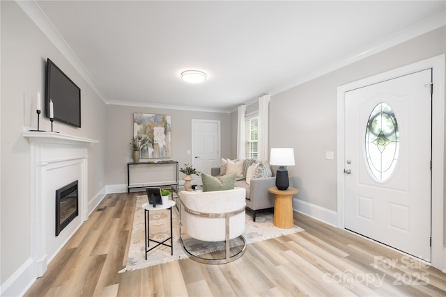 entryway with crown molding, a glass covered fireplace, baseboards, and light wood-style floors