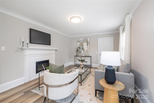living room featuring baseboards, light wood-style floors, crown molding, and a glass covered fireplace