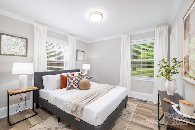 bedroom with visible vents, light wood-type flooring, ornamental molding, and baseboards