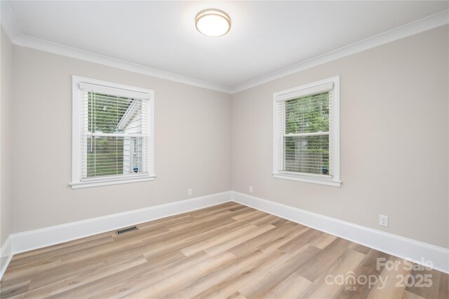 empty room featuring visible vents, wood finished floors, a wealth of natural light, and crown molding