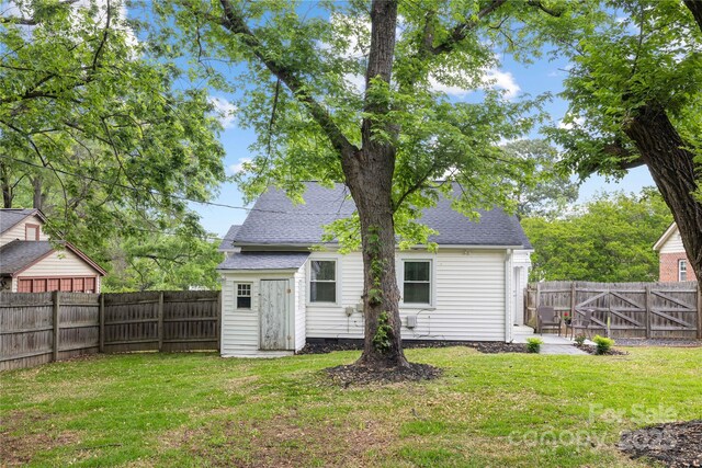 back of property with roof with shingles, a fenced backyard, and a lawn