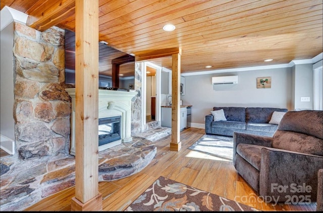 living room featuring baseboards, wood ceiling, wood-type flooring, a glass covered fireplace, and a wall unit AC