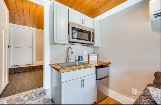 kitchen featuring wooden ceiling, stainless steel microwave, a sink, and fridge