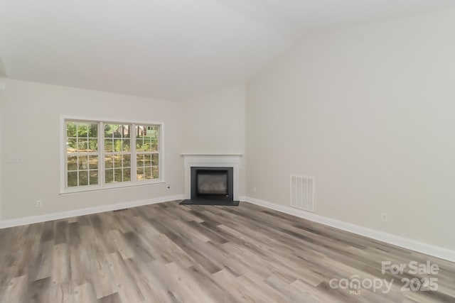 unfurnished living room with a fireplace with flush hearth, visible vents, baseboards, and lofted ceiling