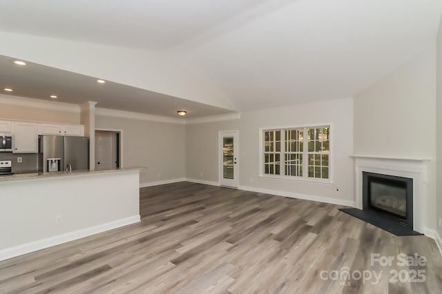 unfurnished living room featuring a glass covered fireplace, baseboards, vaulted ceiling, and wood finished floors
