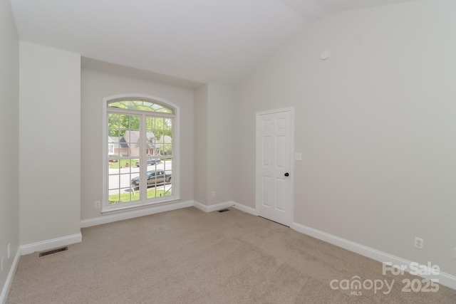 empty room with high vaulted ceiling, light colored carpet, baseboards, and visible vents