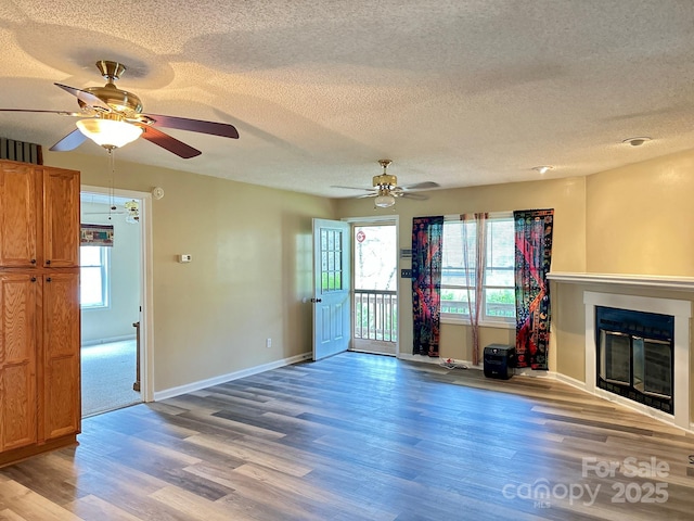 unfurnished living room featuring ceiling fan, light wood finished floors, a glass covered fireplace, and baseboards