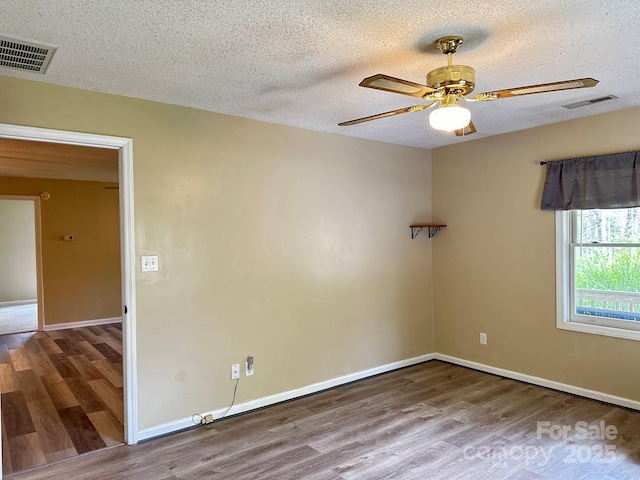 spare room featuring visible vents, a textured ceiling, a ceiling fan, and wood finished floors