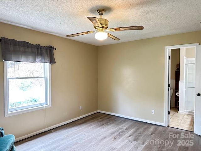 empty room featuring a textured ceiling, wood finished floors, baseboards, and a ceiling fan